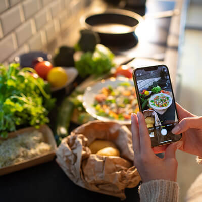 Photo of a woman holding a cell phone taking pictures of food