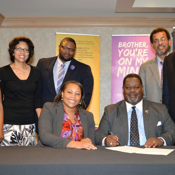 On hand at the signing of the BYOMM agreement are (seated) Dr. Courtney Ferrell Aklin of NIMHD and Antonio F. Knox, Sr. of Omega Psi Phi.