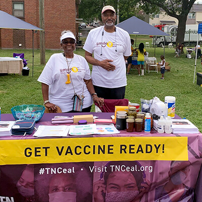 Two African American doctors stand at an intake table at a COVID-19 vaccine site in Tennessee. The table reads ‘GET VACCINE READY!’