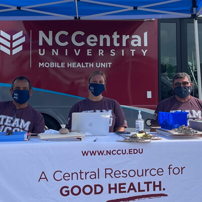Three NCCU team members staff an ACCORD mobile research vehicle at an outdoor event.