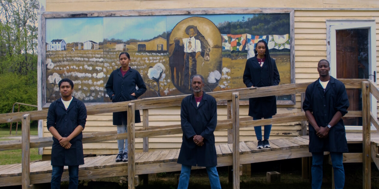 Five scientists standing in front of a museum and mural with arms crossed.