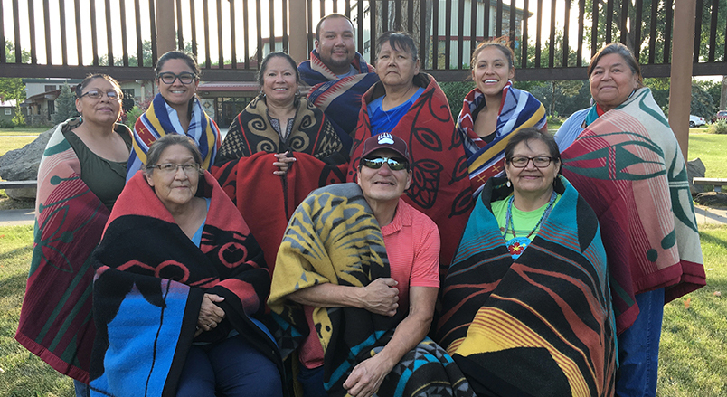 10 people wrapped in Native American blankets pose for a photograph outside. 