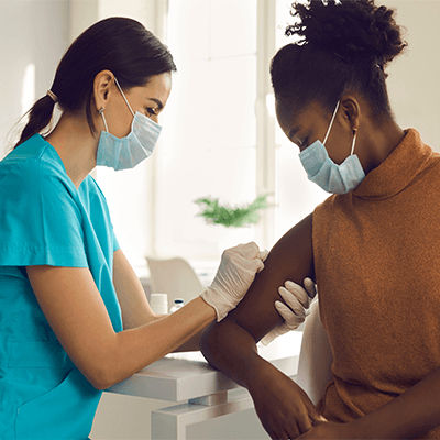 An Asian female nurse preps a Black woman to receive a COVID-19 vaccine.