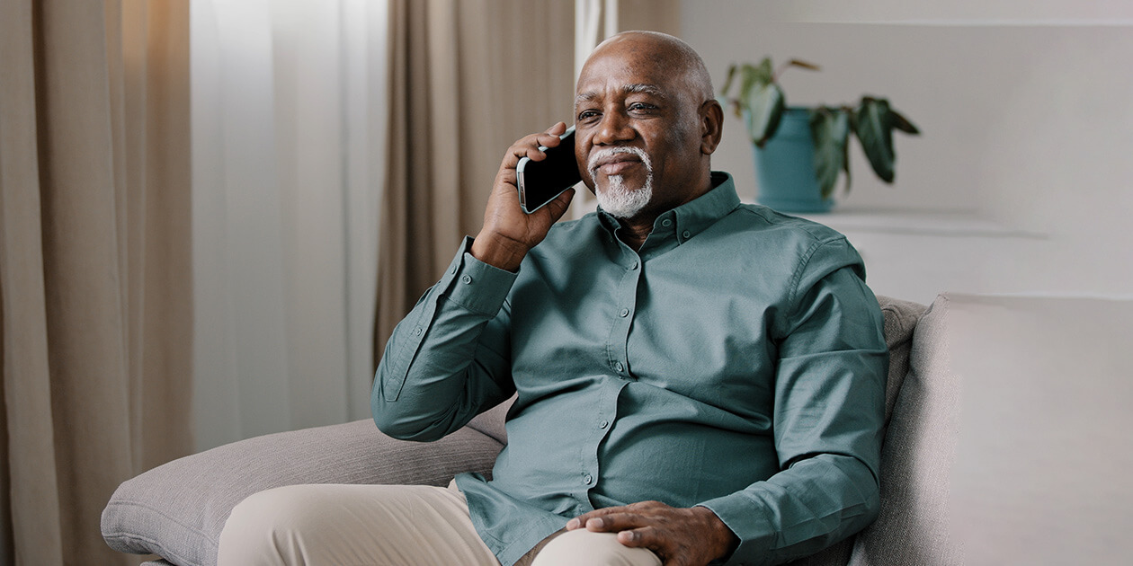 A Black older man sitting on a couch and holding a cell phone to his right ear