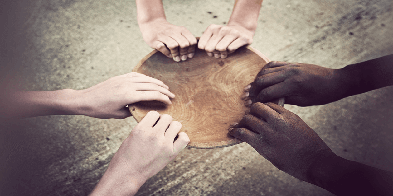 3 pairs of hands of different skin colors grasp the rim of an empty bowl