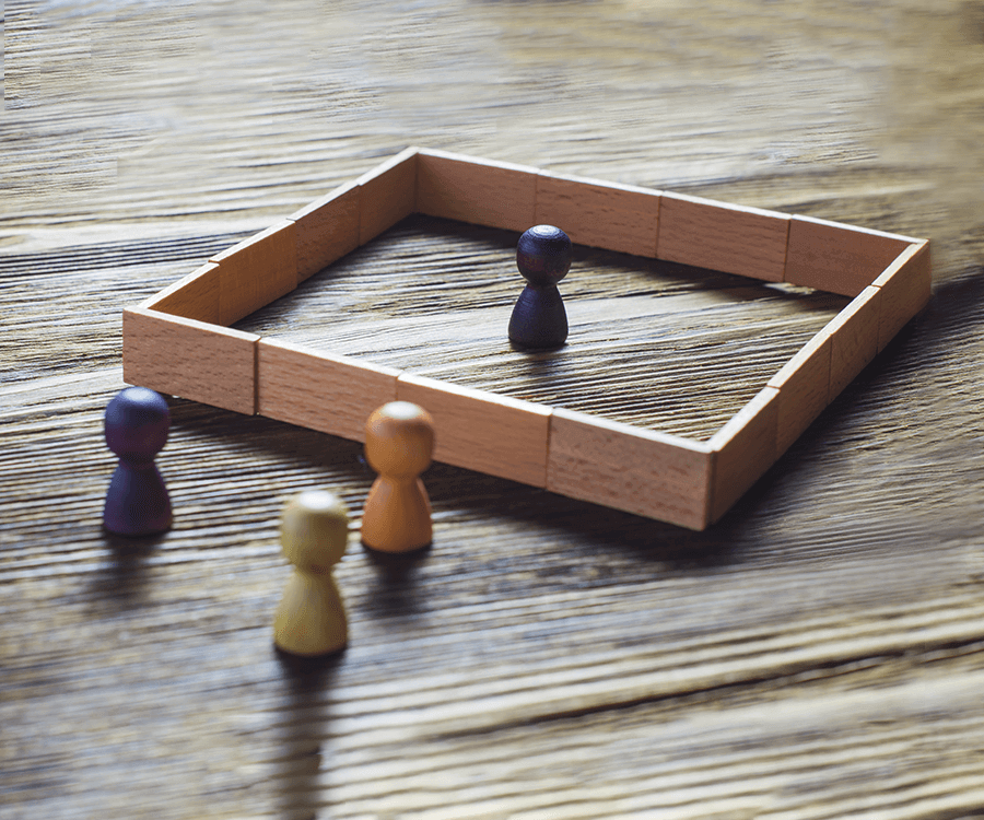 Abstract image representing SRD, darker wooden figure in a box with three other wooden figures in light, medium and dark shades outside the box