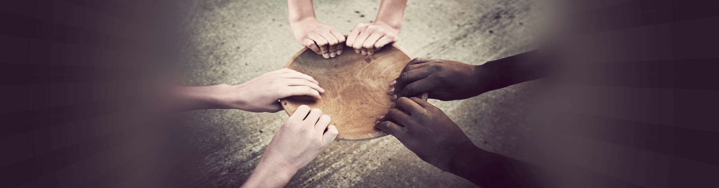 3 pairs of hands of different skin colors grasp the rim of an empty bowl